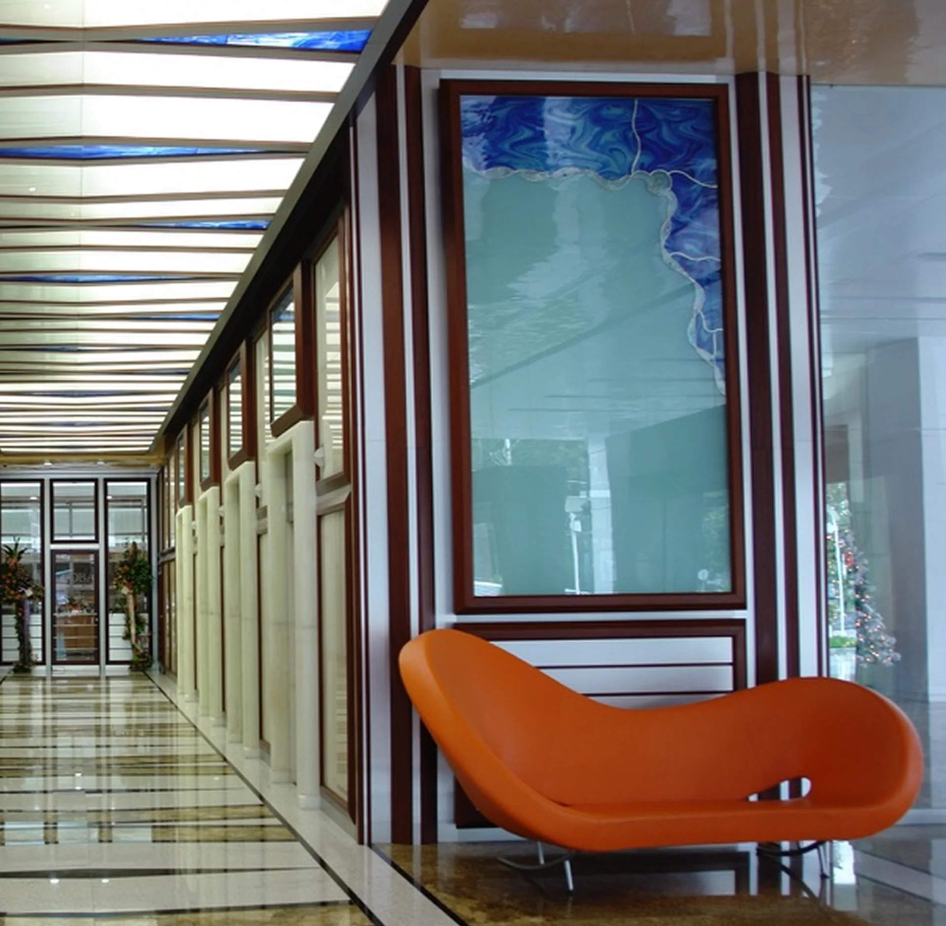 Galería de acceso con paneles de ónice retroiluminado, vidrio artístico azul y butaca naranja