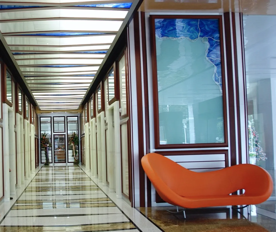 Pasillo con techo de cristal azul retroiluminado, mármol pulido y chaise longue naranja