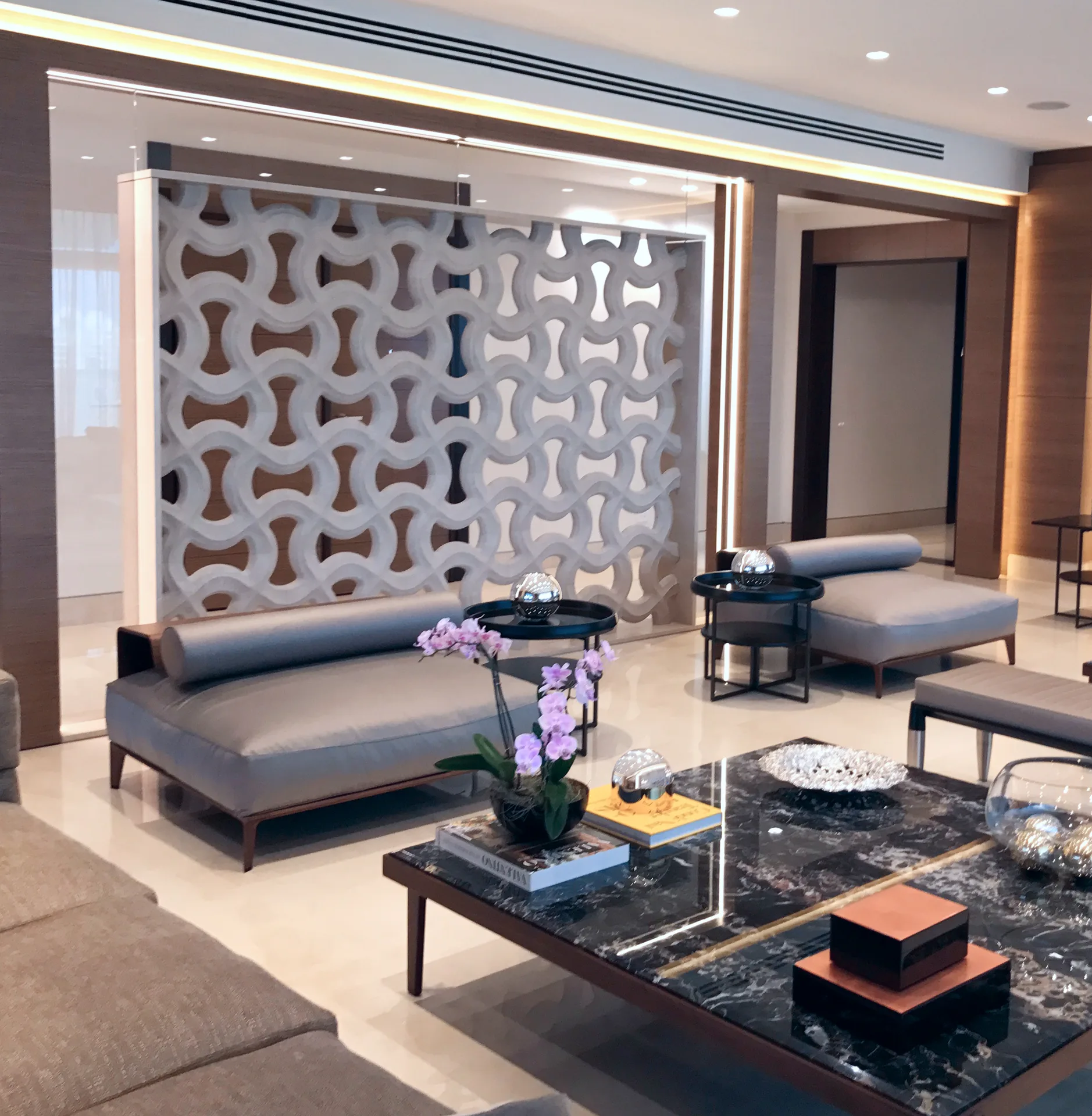 Salón con celosía escultórica en mármol, chaise longues y mesa en Negro Marquina