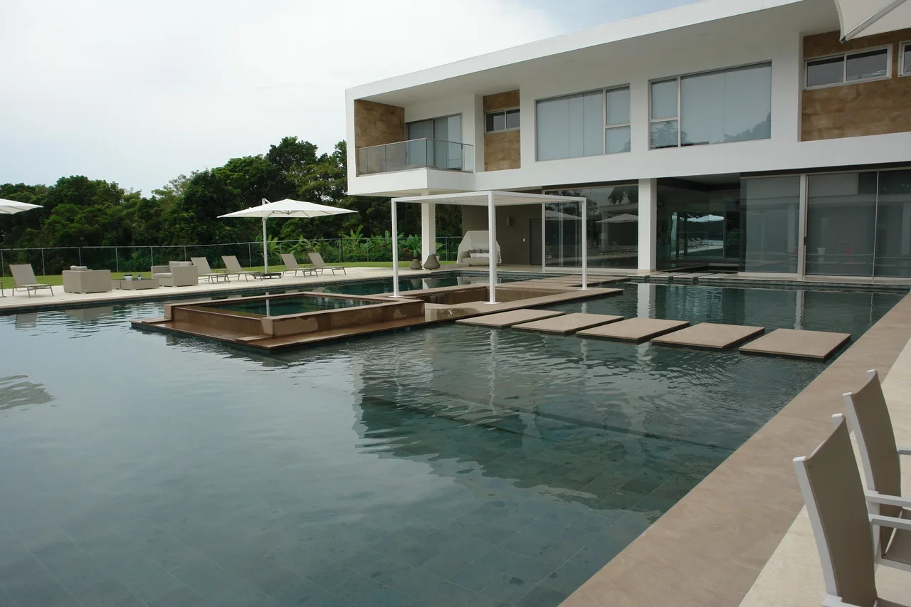 Villa con piscina y pasarela de piedra sobre el agua, obra terminada