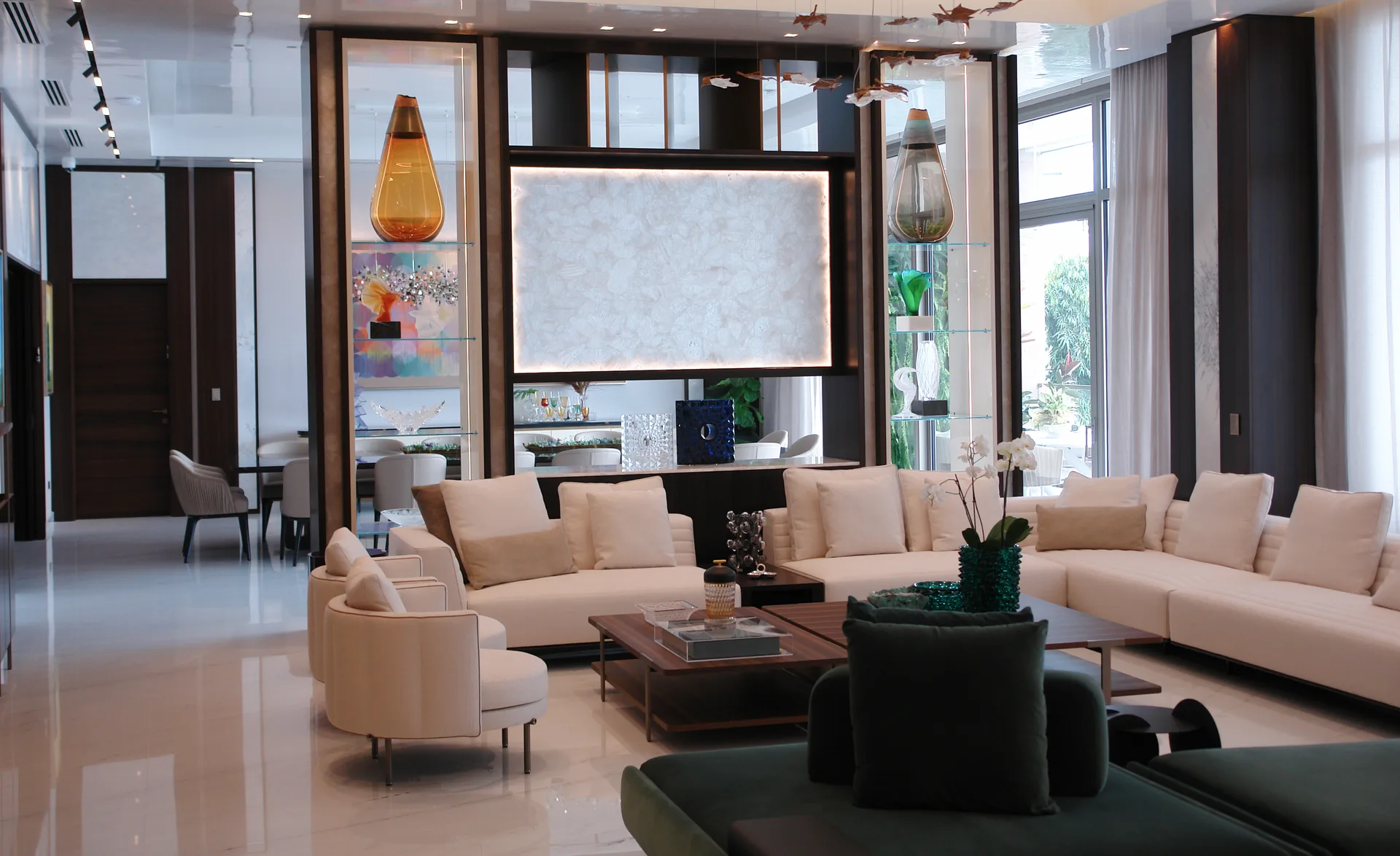 Salón de doble altura con sofás en crema, lámparas de cristal soplado y panel retroiluminado de ónix