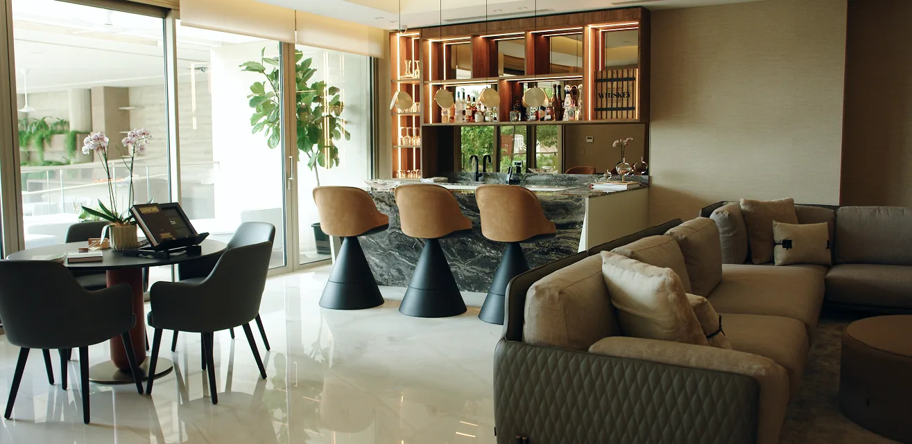 Salón con barra en mármol, taburetes de cuero y ventanales al jardín